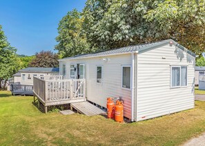 Ein eingeschossiges Mobilheim mit einer Terrasse, einer kleinen Veranda und Propangasbehältern.