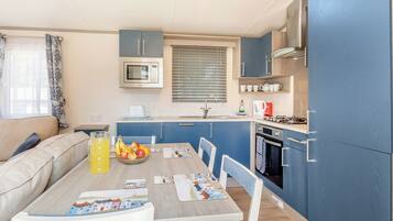 A compact kitchen with a microwave, stove, and sink. There's a dining table with chairs and a bowl of fruit.