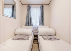 Ein Doppelzimmer mit zwei Betten, einem Spiegel und einem Fenster mit Vorhängen.
