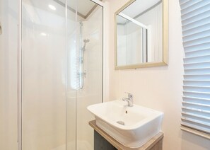 A bathroom with a glass shower enclosure, a white sink, and a mirror on the wall.