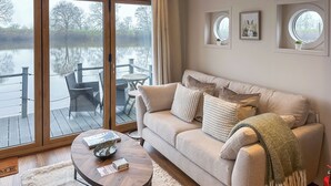 A living room with a sofa, a coffee table, and a view of a lake through large sliding glass doors. - 1 bedroom accommodation in Naburn, York (Naburn, York)