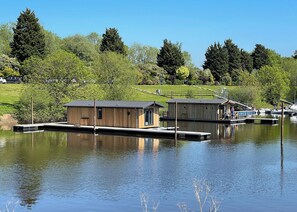A lakeside property with wooden cabins, docked boats, and a grassy landscape.