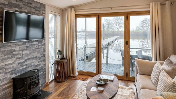 A living room with a fireplace, a sofa, a coffee table, a TV, and a view of a dock and water. - 1 bedroom accommodation in Naburn, York (Naburn, York)