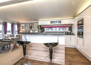 A modern kitchen with a central island, bar stools, and a dining area with a view. - 2 bedroom accommodation in Carnforth (Carnforth)