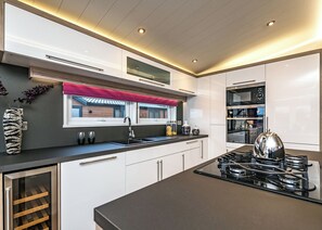 A modern kitchen with a central island, built-in appliances, and a window with a red valance.