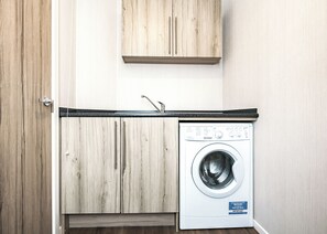 A compact laundry room with a washing machine, wooden cabinets, and a countertop.