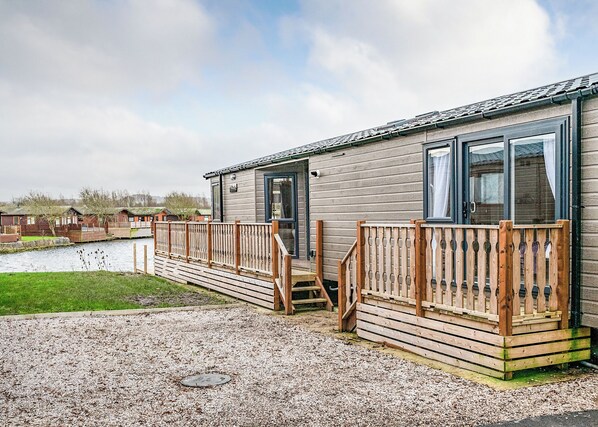 A single-story mobile home with a wooden deck, a small outdoor area, and a view of a water body.