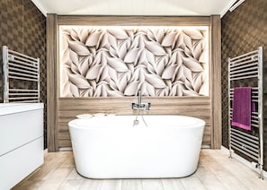 Un baño moderno con una bañera independiente, revestimiento de madera y dos toalleros.