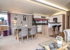A modern kitchen with a dining area, featuring a glass table, grey chairs, and a small island. - 2 bedroom accommodation in Carnforth (Carnforth)