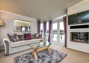 A modern living room with a glass coffee table, a sofa with patterned cushions, a large mirror, and a fireplace. - 2 bedroom accommodation in Carnforth (Carnforth)