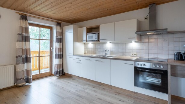 Una cucina moderna con pavimento in legno, mobili bianchi, forno in acciaio inossidabile e una finestra con tende.