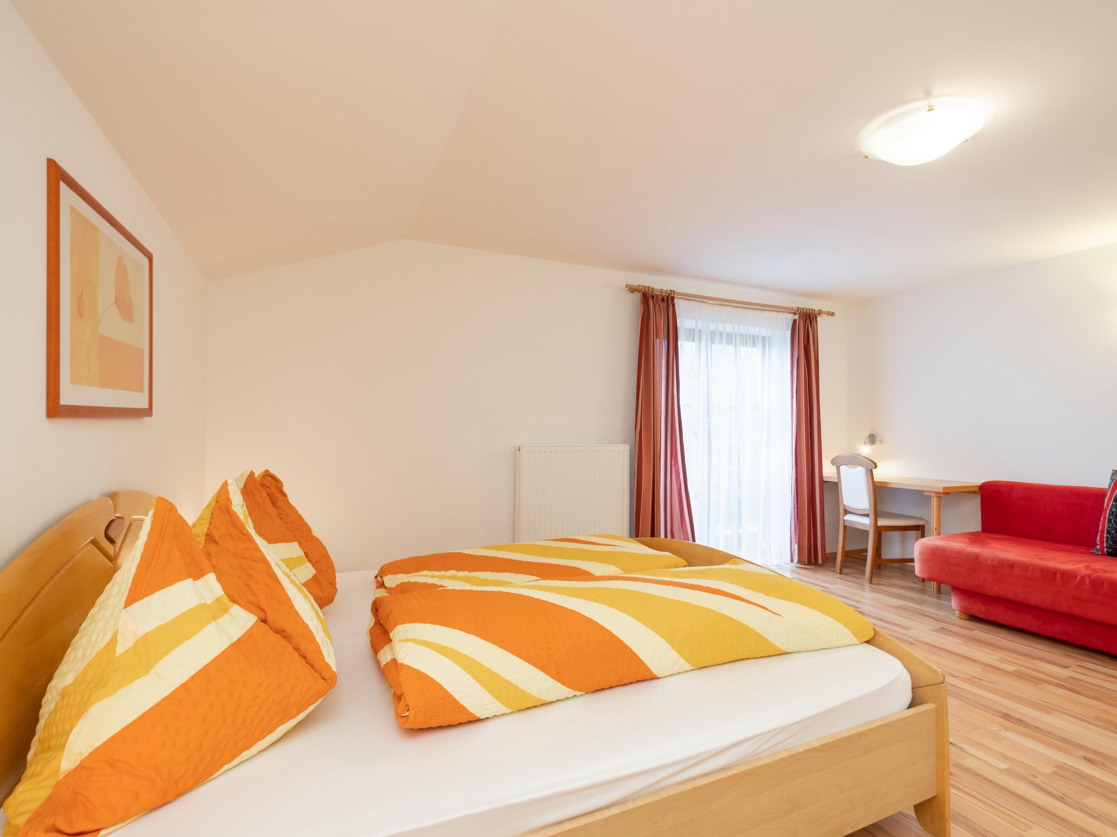 Ein Hotelzimmer mit einem Bett, einem Schreibtisch, einem Stuhl und einem roten Schlafsofa.