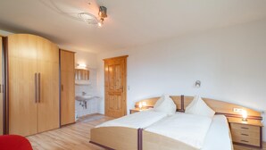 Una camera da letto con un letto di legno, una sedia rossa, un armadio di legno, una porta in legno e un bagno con lavandino e specchio.
