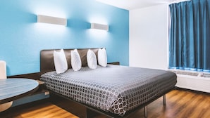 A hotel room with a bed, a round table, and a window with curtains. - Blue Way Inn Fairmont (Fairmont)