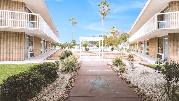 A modern building with a central walkway leading to a covered area, surrounded by greenery and palm trees. - Blue Way Inn Fairmont (Fairmont)