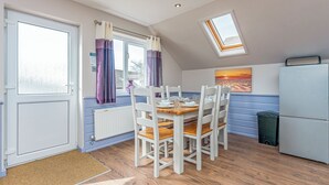 A kitchen with a dining table, chairs, a refrigerator, a window with curtains, a radiator, and a skylight.