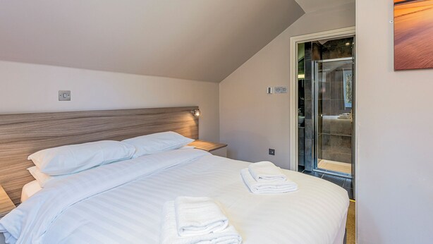A modern hotel room with a wooden headboard, a neatly made bed, a glass shower door, and a painting on the wall.