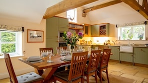 A dining area with a wooden table set for four, surrounded by green cabinets and a kitchen in the background.