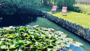 A serene garden with a pond, lush greenery, and two red and white striped chairs. - Detached Cotswold converted Barn near Chipping Campden (gloucestershire)