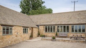 A stone building with a large window and a bench in the courtyard. - Detached Cotswold converted Barn near Chipping Campden (gloucestershire)