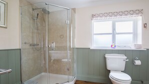 Un baño con cabina de ducha de vidrio, inodoro y ventana con cortina.