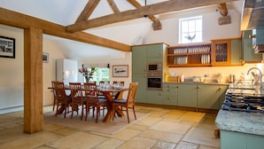 A kitchen with a dining area, featuring wooden beams, green cabinets, and a tiled floor. - Detached Cotswold converted Barn near Chipping Campden (gloucestershire)