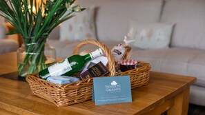 Una cesta de mimbre con una botella de vino verde, barras de chocolate y un tarro de mermelada sobre una mesa de madera.