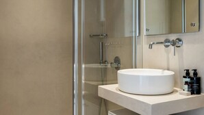 Ein modernes Badezimmer mit einer gläsernen Duschkabine, einem weißen Waschbecken und einem Spiegel darüber.