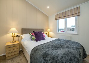 A bedroom with a bed, two bedside tables, a window with a view, and a radiator.