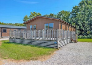 A single-story wooden building with a fenced porch, a gravel driveway, and a grassy area.