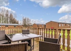 A deck with wicker furniture and a view of mobile homes in the background.