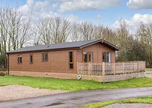 A wooden cabin with a balcony, a gravel driveway, and a grassy area.