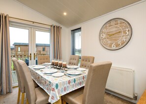 Un comedor con una mesa dispuesta para cuatro personas, un reloj de pared grande y vistas a través de la ventana.