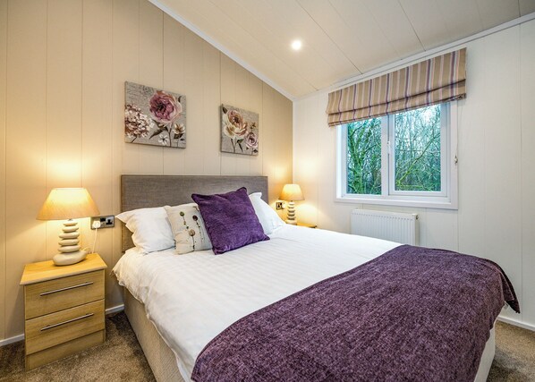 Quarto com cama, duas luminárias de parede, janela com cortinas e duas peças de arte floral.