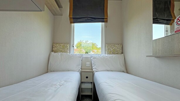 A small, single-room accommodation with two beds, a window, and a mirror. - Honeysuckle Prestige (Chapel St Leonards, Skegness)