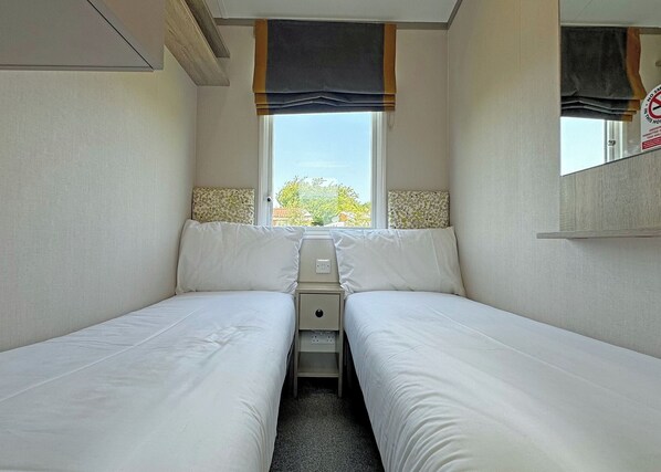 A small, single-room accommodation with two beds, a window, and a mirror.