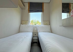 A small, single-room accommodation with two beds, a window, and a mirror.