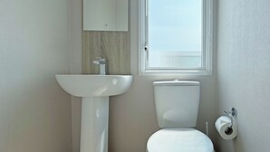 A bathroom with a white sink, toilet, and window. - Honeysuckle Prestige (Chapel St Leonards, Skegness)