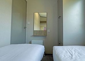 A hotel room with two beds, a mirror, a radiator, and a door.