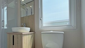 Une salle de bain avec un meuble-lavabo en bois, un lavabo blanc, un miroir, des toilettes et une fenêtre avec des stores.