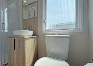 A bathroom with a wooden vanity, a white sink, a mirror, a toilet, and a window with blinds.