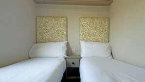 A small, single-room accommodation with two single beds, a nightstand, and a wall-mounted power outlet. - Honeysuckle Prestige (Chapel St Leonards, Skegness)
