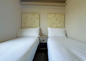 A small, single-room accommodation with two single beds, a nightstand, and a wall-mounted power outlet. - Honeysuckle Prestige (Chapel St Leonards, Skegness)