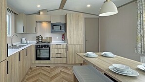 A compact kitchen with a microwave, stove, sink, and wooden cabinets. - Honeysuckle Prestige (Chapel St Leonards, Skegness)