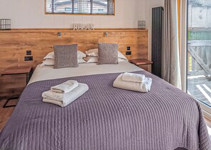A hotel room with a wooden headboard, a bed with a purple quilt, two pillows, and two towels on the bed.