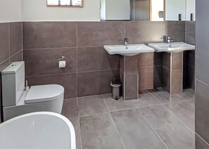 A modern bathroom with a toilet, two sinks, a trash bin, and a mirror.