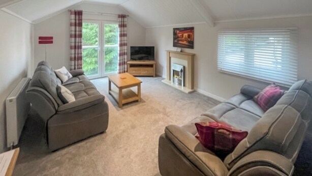 A spacious loft-style living room with a high ceiling, two sofas, a coffee table, a fireplace, and a TV. - 3 bedroom accommodation in Milnthorpe (Milnthorpe)