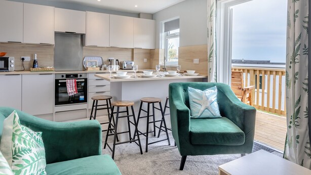 Une cuisine moderne avec un îlot central, des tabourets de bar et un fauteuil vert.