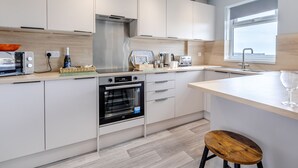 A modern kitchen with white cabinets, a built-in oven, a microwave, a kettle, and a toaster.