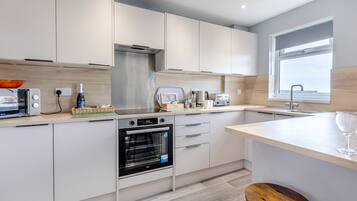 A modern kitchen with white cabinets, a built-in oven, a microwave, a kettle, and a toaster.